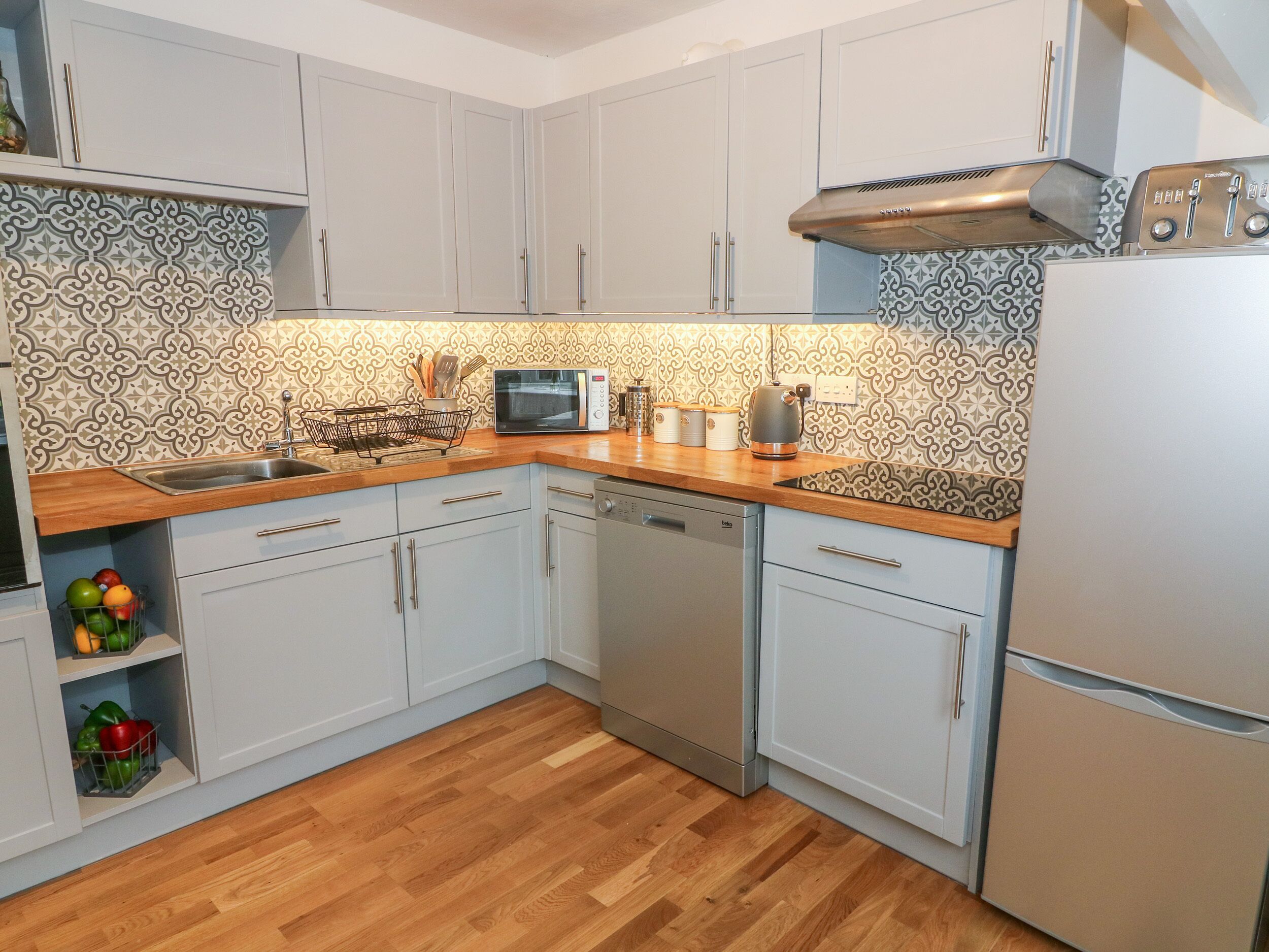 A kitchen with white cabinets, a microwave, a kettle, and a dishwasher.