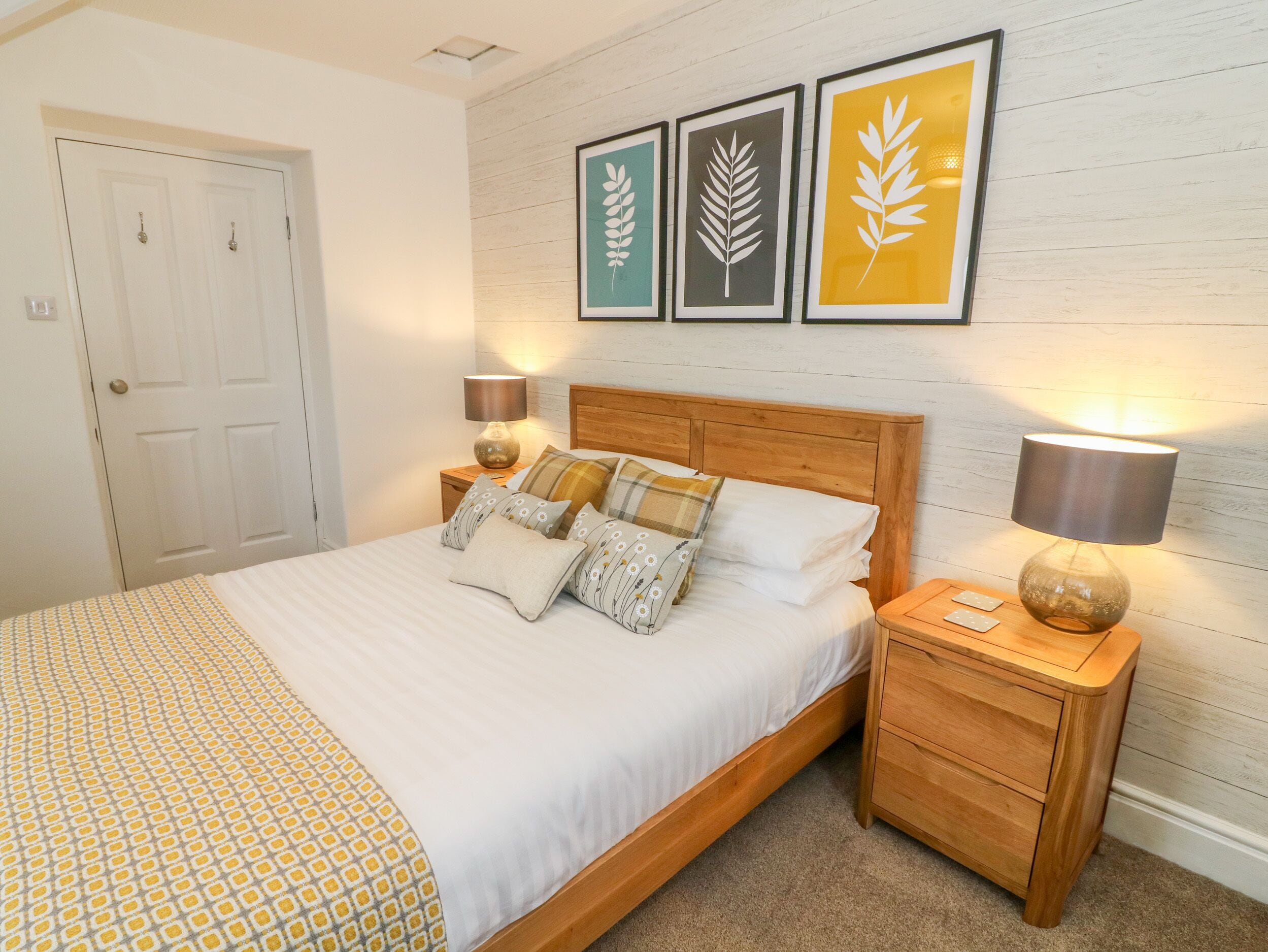 A neatly made bed with patterned bedding, two bedside tables with lamps, and three framed wall art pieces above the bed.