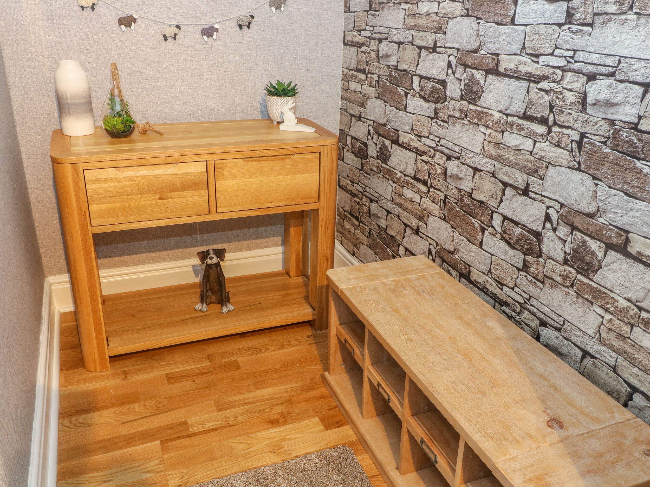 Una consola de madera con una figurita de perro, una planta pequeña en maceta y objetos decorativos encima.