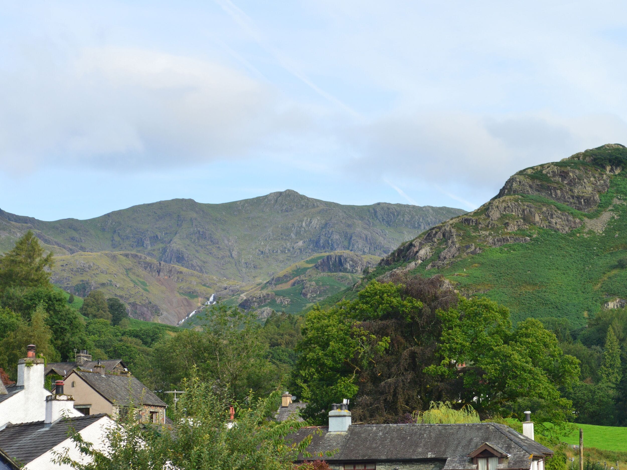 Un paysage montagneux avec des maisons au premier plan et une cascade dans la vallée.