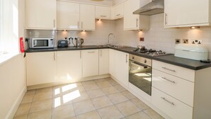 A modern kitchen with white cabinets, a black countertop, and a green pendant light. - Tirionfa (Llangefni)