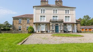 A large, two-story stone building with a symmetrical facade, a central entrance with a decorative arch, and a gravel driveway leading to the entrance. - Tirionfa (Llangefni)