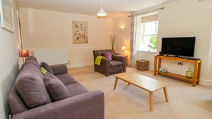 A living room with a sofa, armchair, coffee table, TV, and lamp. - Tirionfa (Llangefni)