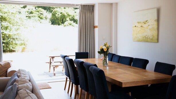Ein stilvolles Esszimmer mit Holztisch und dunklen Stühlen, einer Blumenvase und Blick ins Grüne.