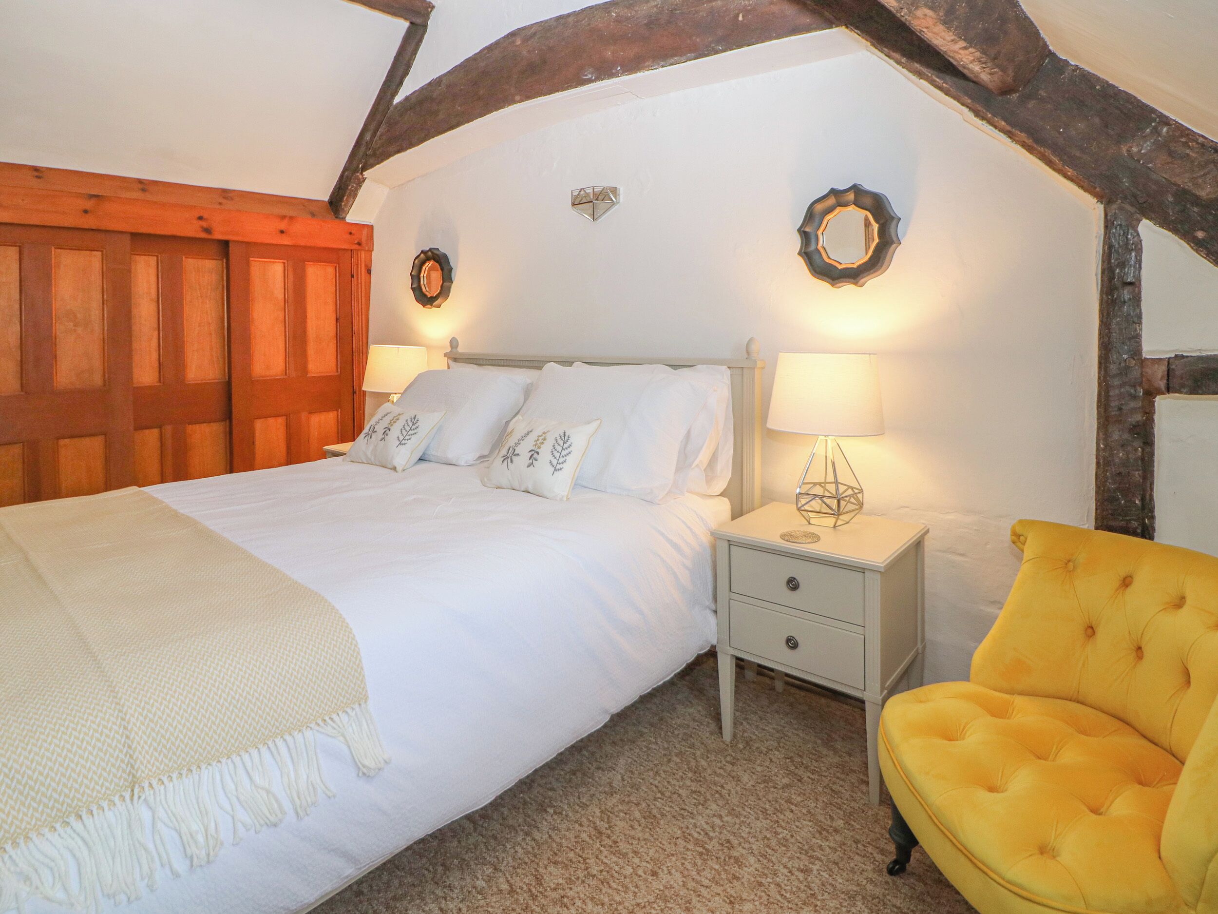 Une chambre à coucher comprenant un lit, des tables de chevet, une commode, une chaise et une poutre en bois au plafond.