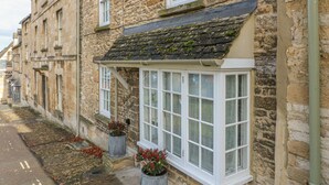 Un bâtiment en pierre à l’architecture traditionnelle, doté de nombreuses fenêtres et d’un petit porche agrémenté de plantes en pot.
