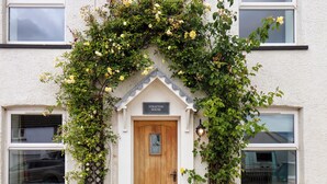 Una casa con puerta de madera, un letrero encima de la puerta y una pared blanca.