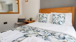 Habitación de hotel con cama, una silla, una mesita de noche, un espejo y un enchufe.