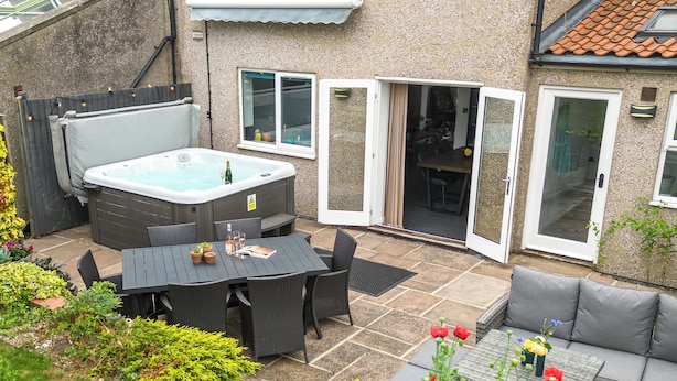 Un patio con jacuzzi, mobiliario de exterior y diversas plantas.