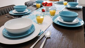Una mesa de desayuno dispuesta con platos, tazones y vasos de zumo de naranja, todo en tonos azul y blanco.