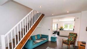 Una sala de estar moderna con un sofá azul turquesa, una escalera de madera y una cocina al fondo.