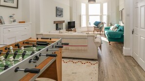 A spacious living room with a foosball table, a sofa, and a teal armchair. - 11 Marine Terrace (Criccieth)
