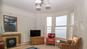 A living room with a fireplace, a television, a striped armchair, and a view of the sea through large windows. - 11 Marine Terrace (Criccieth)
