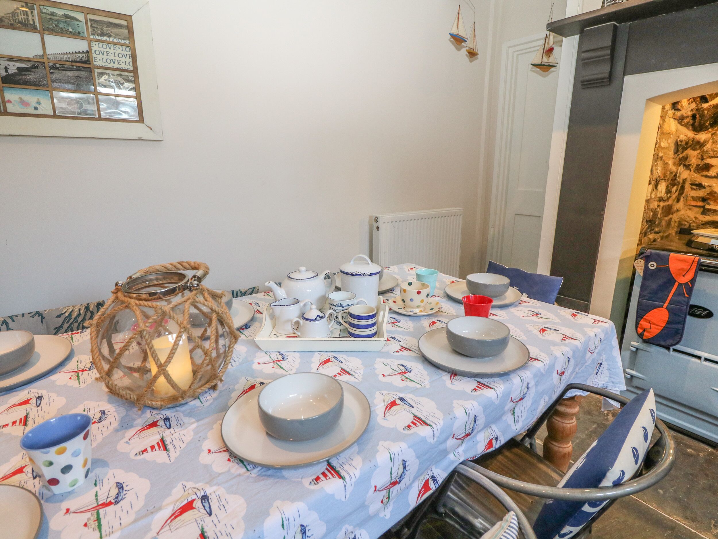 Une table à manger dressée avec de l’assiette blanche, des bols et des théières, le tout posé sur une nappe à motifs marins.