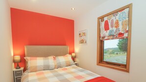 Un dormitorio con pared roja, colcha a cuadros, dos lámparas de noche y una ventana con vistas al exterior.