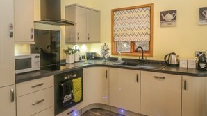 Una cocina moderna con microondas, horno y fregadero. Hay armarios, una ventana con cortina estampada y una cafetera sobre la encimera.