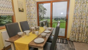 Un comedor con una mesa dispuesta para cuatro personas, sillas, un camino de mesa amarillo y vistas a un paisaje verde a través de un ventanal.