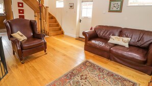 A spacious living room with a wooden staircase, leather armchair, leather sofa, and a patterned rug. - The Shippon (Tarporley)