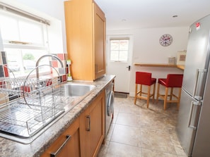 A kitchen with a stainless steel sink, wooden cabinets, a built-in washing machine, and a refrigerator. - The Shippon (Tarporley)
