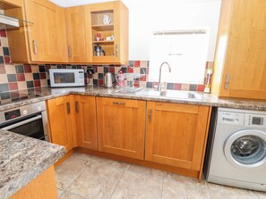 A kitchen with wooden cabinets, a microwave, a coffee maker, and a washing machine. - The Shippon (Tarporley)
