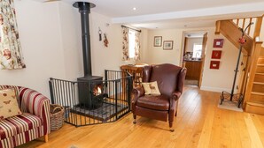 A cozy living room with a fireplace, a striped sofa, a leather armchair, and a wooden floor. - The Shippon (Tarporley)