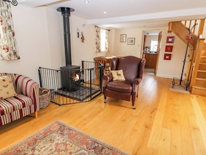A cozy living room with a fireplace, a striped sofa, a leather armchair, and a wooden floor. - The Shippon (Tarporley)