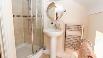 A bathroom with a glass-enclosed shower, a pedestal sink, a round mirror, and a towel rack with a towel.