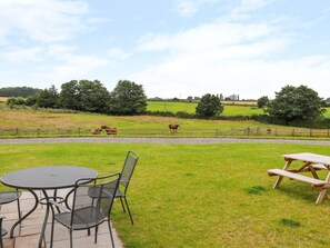 A patio area with a round table and chairs, a picnic table, and a view of horses grazing in a field. - The Shippon (Tarporley)