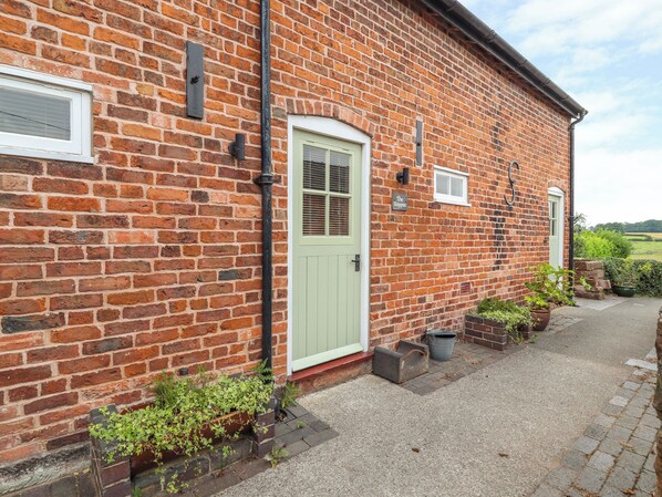 A brick building with a light green door, a small window, and a sign that reads "The Shoppin". - The Shippon (Tarporley)