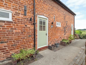 A brick building with a light green door, a small window, and a sign that reads "The Shoppin". - The Shippon (Tarporley)