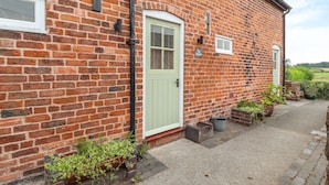 A brick building with a light green door, a small window, and a sign that reads "The Shoppin". - The Shippon (Tarporley)