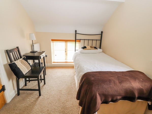 A small, well-lit room with a single bed, a desk with a chair, and a window with blinds. - The Shippon (Tarporley)