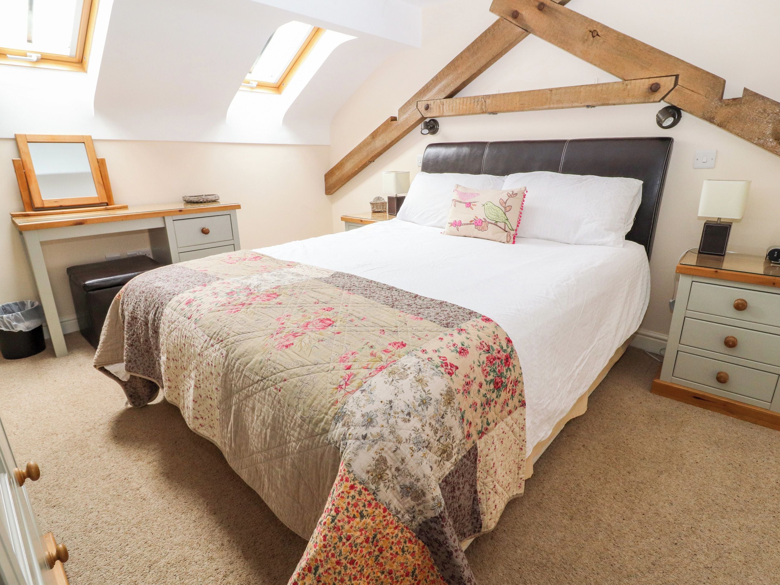 A bedroom with a large bed, a desk, and a chair. There is a skylight above the bed.