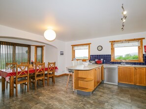 A compact kitchen with wooden cabinets, a dining table with chairs, a built-in island, and a window with a view.