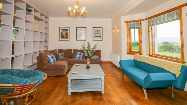 A living room with a brown sofa, blue sofa, wicker chair, white coffee table, and a bookshelf. - Ptarmigan (Grantown-on-Spey)