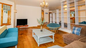 A living room with a television, a coffee table, a blue sofa, a brown sofa, and a bookshelf. - Ptarmigan (Grantown-on-Spey)