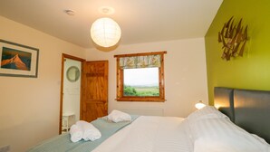 A bedroom with a bed, a window with a view, a mirror, and a framed picture on the wall. - Ptarmigan (Grantown-on-Spey)