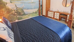 Ein Schlafzimmer mit einem großen Bett, einem Holztisch, einem Kleiderschrank und Blick auf eine Küstenlandschaft.