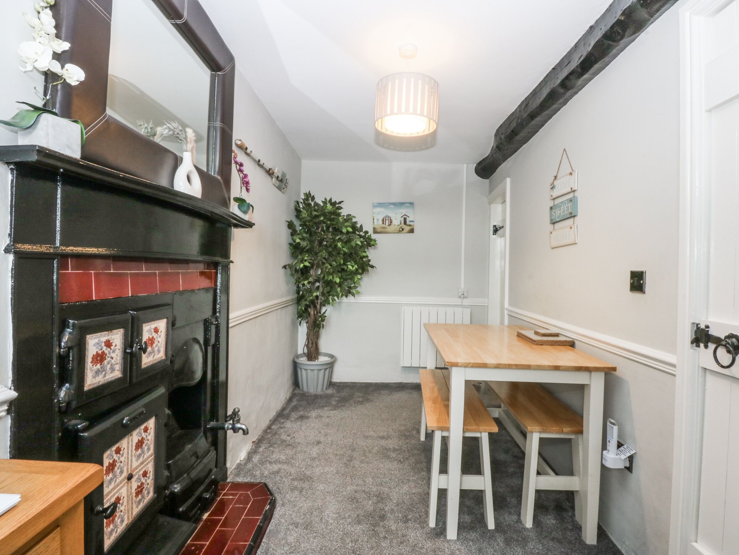 A narrow kitchen with a black stove, white cabinets, a wooden table, and a hanging light fixture.