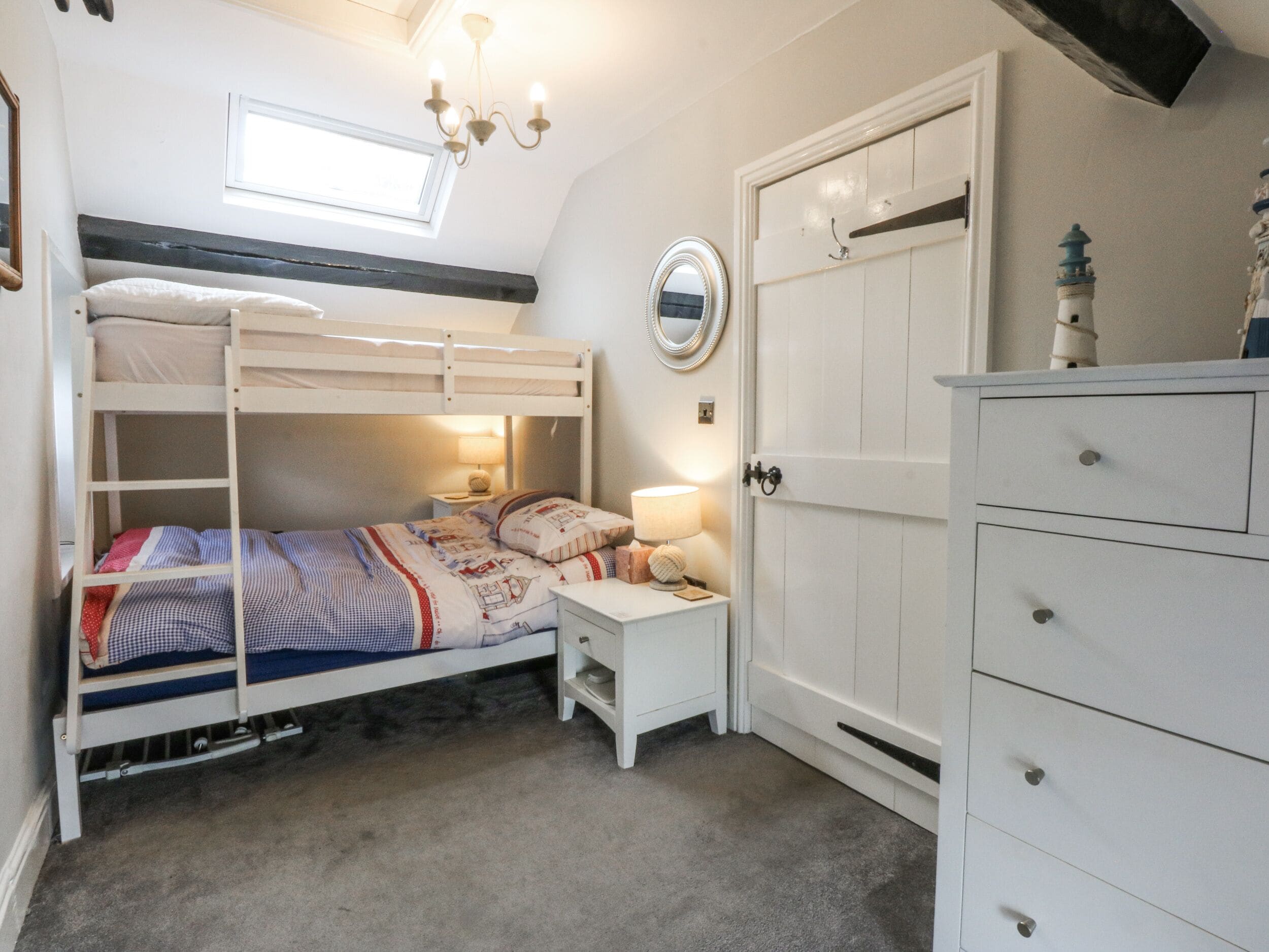 A bunk bed with a nightstand, a dresser, a mirror, and a chandelier.