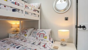 A bedroom with a bunk bed, a bedside table with a lamp, a mirror, and a decorative item on the nightstand. - Tan Yr Allt (Pwllheli)
