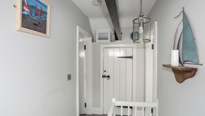 A hallway with a white door, a ceiling light, a framed painting, and a small shelf with a sailboat decoration. - Tan Yr Allt (Pwllheli)
