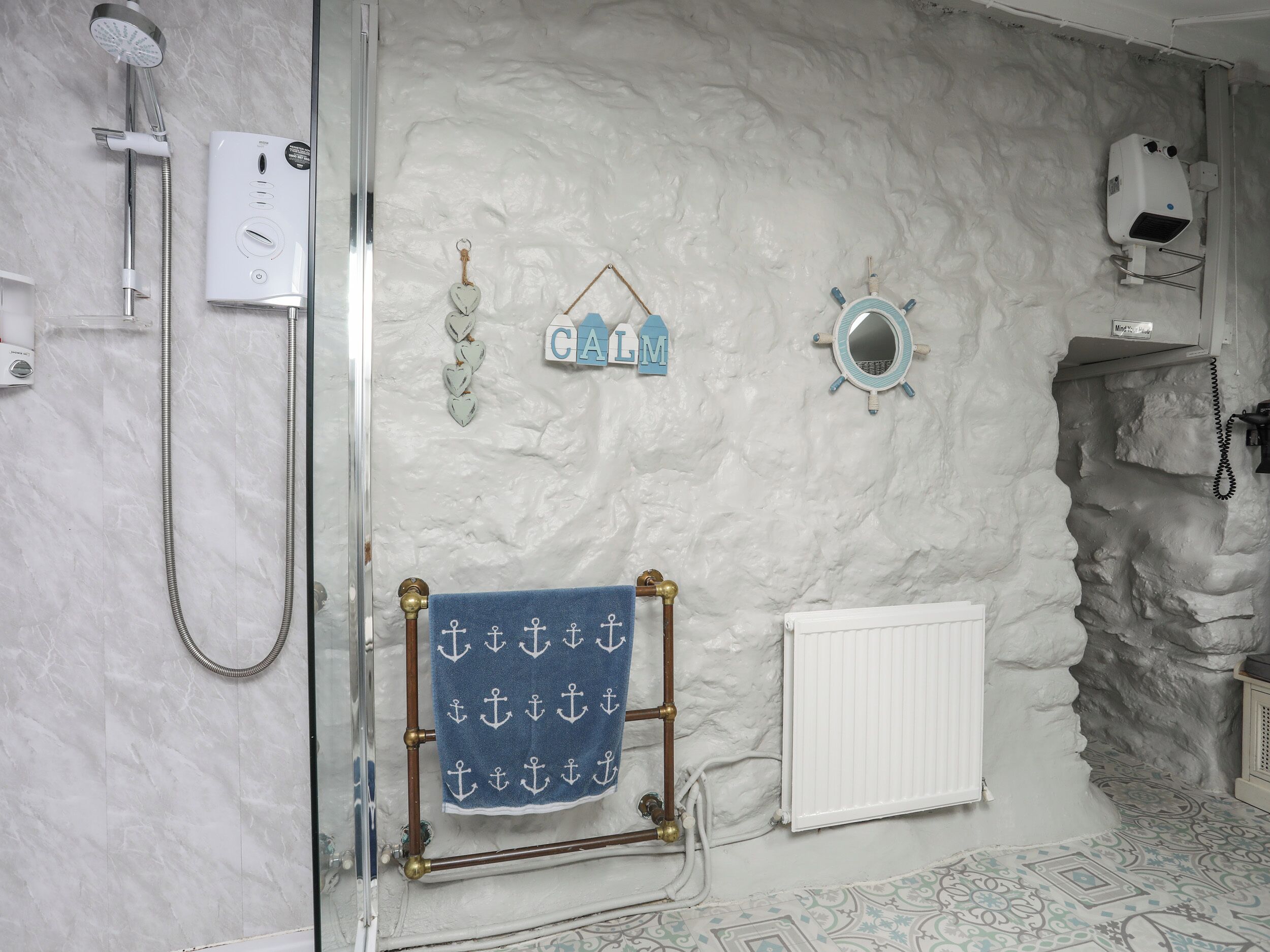 A bathroom with a shower, a towel rack with a blue towel, a radiator, and a decorative wall with a 'CALM' sign.