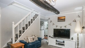 A living room with a blue sofa, a white entertainment unit, a TV, a lamp, and a staircase. - Tan Yr Allt (Pwllheli)