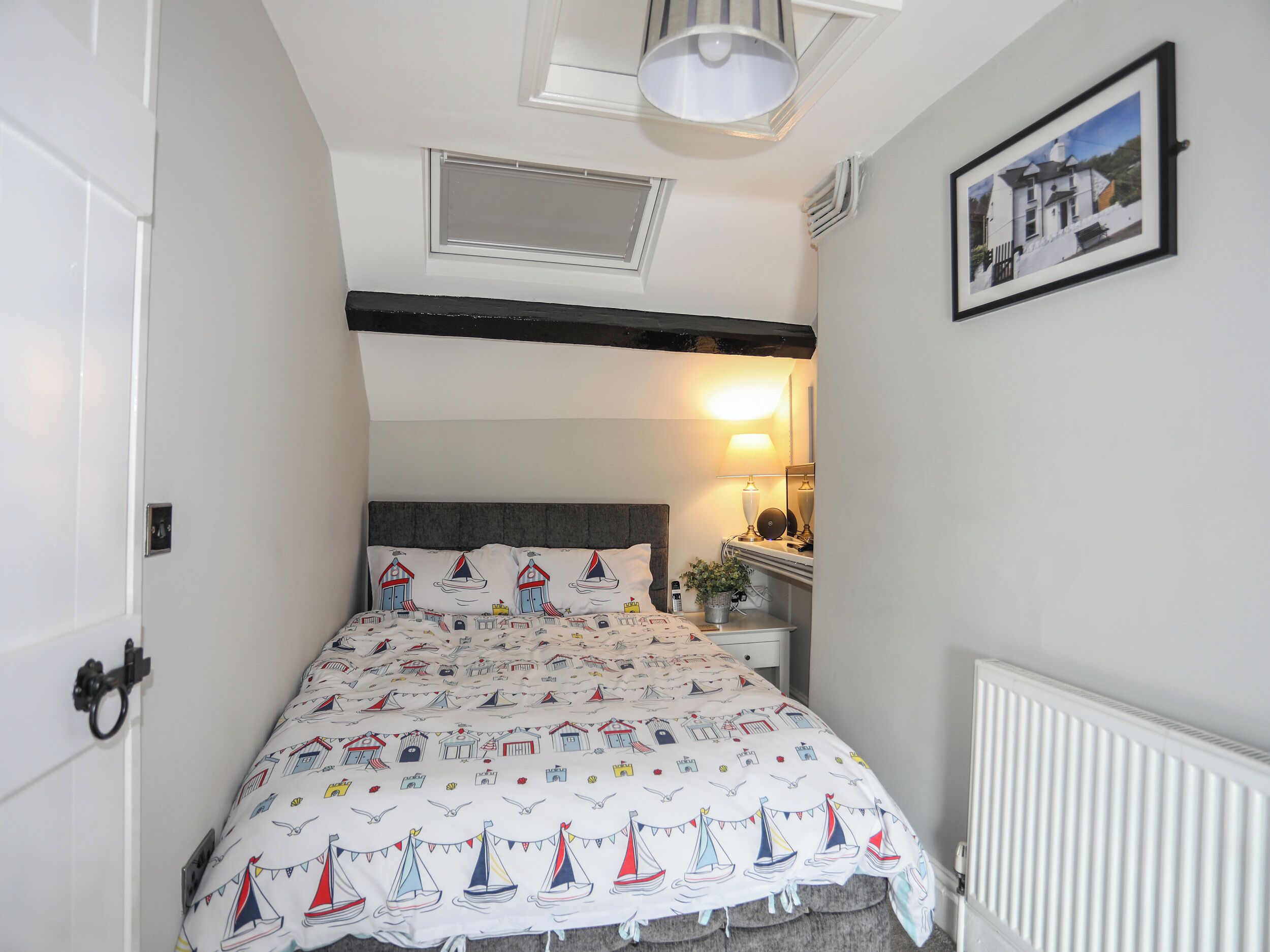 A bedroom with a bed, a nightstand, a lamp, a framed picture on the wall, and a window with blinds.