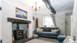 A living room with a fireplace, a blue sofa, and a chandelier. - Tan Yr Allt (Pwllheli)