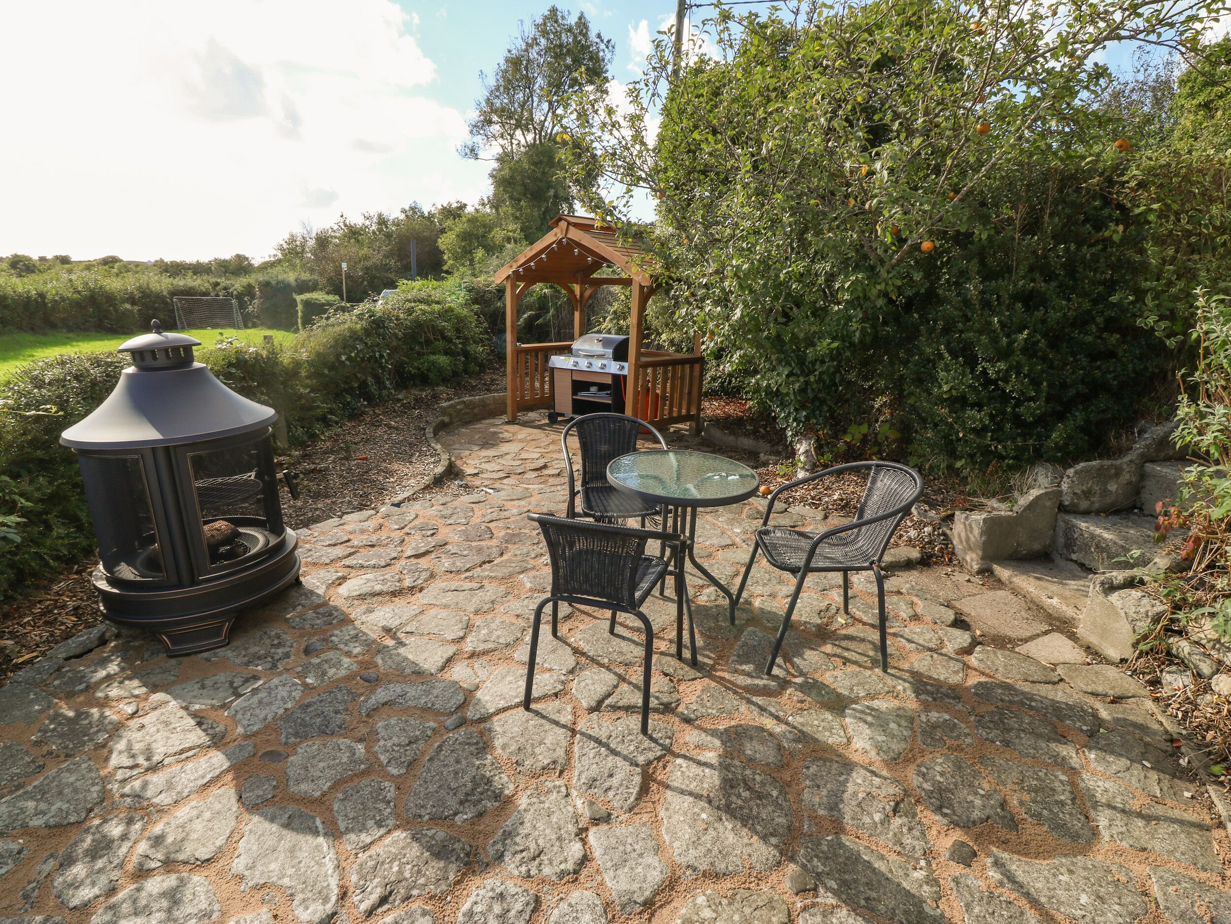 A stone patio with a grill, two chairs, and a lantern.