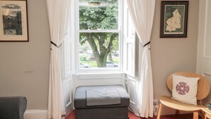 Una habitación con ventanal, un mapa enmarcado, un banco pequeño y una silla.