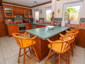 A kitchen with wooden cabinets, a green countertop, and a breakfast bar with bar stools. - Coth Skyber (Hayle)