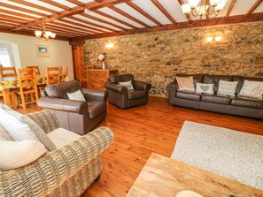 A cozy living room with leather sofas, a wicker chair, and a stone wall. - Coth Skyber (Hayle)